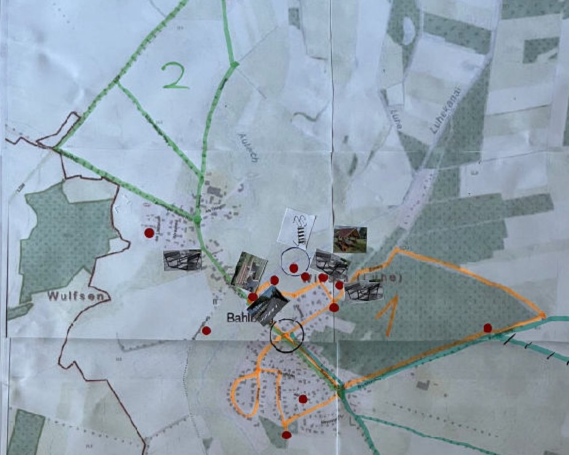 Photograph of a working map from the village workshop: three circular routes drawn in colour on a hiking map, with red dots and photographs attached.